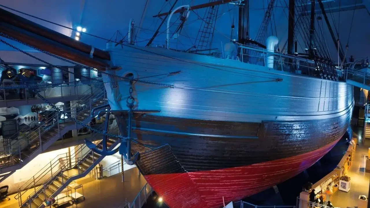 Ein historisches **fram schiff** mit Anker, umgeben von Treppen und Ausstellungsbereichen, in blauem Licht.