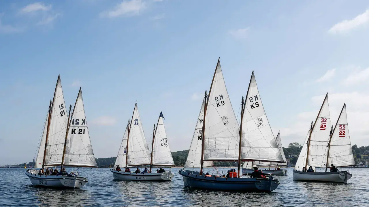 Segelboote mit weißen Segeln und Nummern wie "21" und "K9" auf dem Wasser, ein Teil der Veranstaltung "wm kiel".