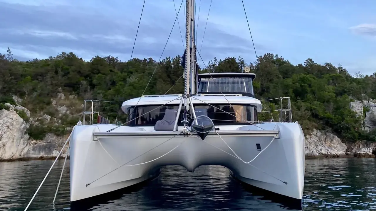 Ein moderner Katamaran mit zwei Rümpfen, der wie ein schwimmendes Haus aussieht, ankert vor einer bewaldeten Küste.