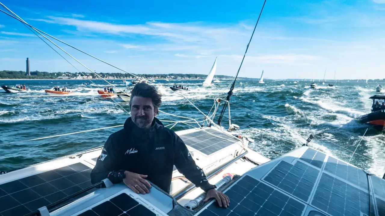 Boris Herrmann in Kiel, auf seinem Boot mit Solarpaneelen, umgeben von anderen Booten und Segelschiffen auf dem Meer.