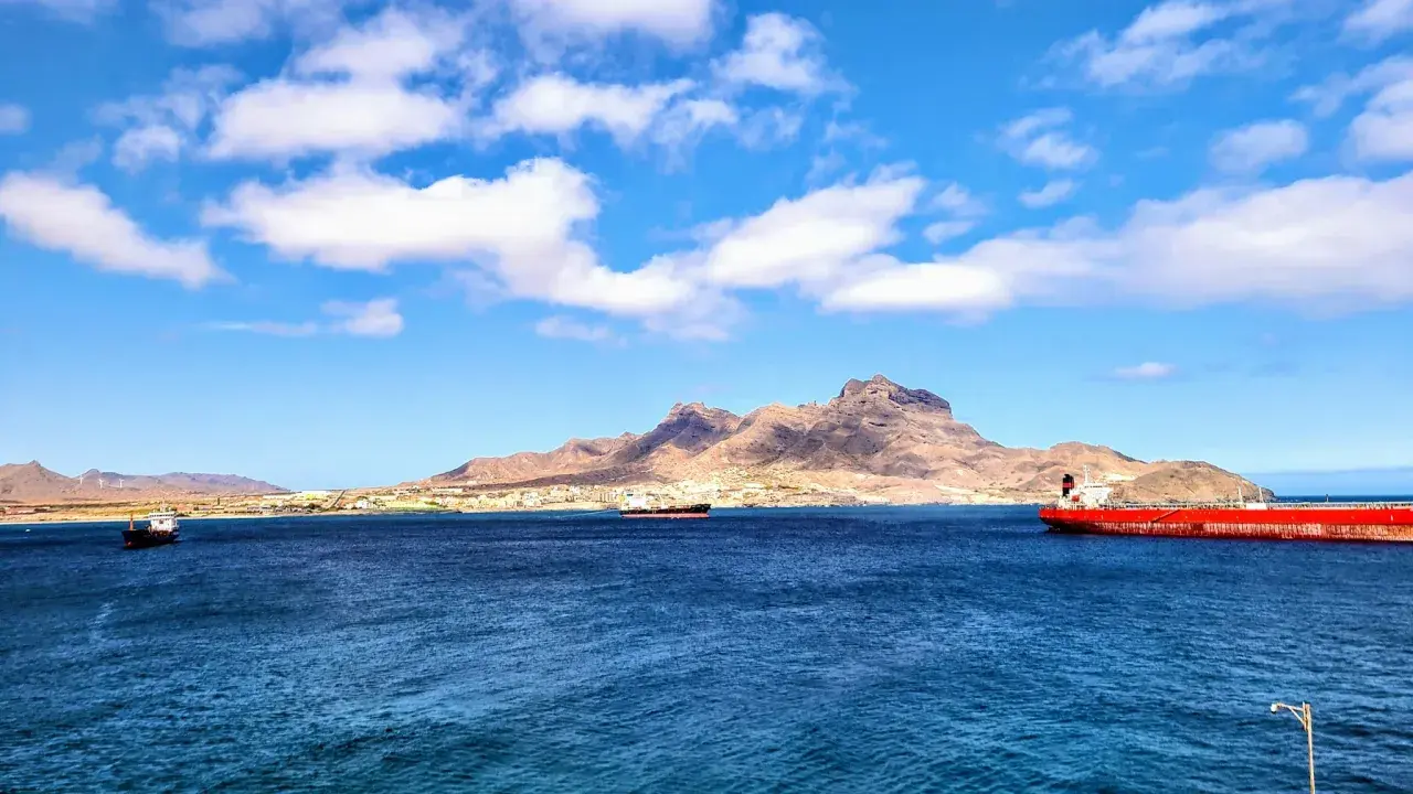 Blick auf die Bucht von Mindelo, Kap Verde, mit Schiffen im tiefblauen Wasser und einer bergigen Küstenlinie im Hintergrund.