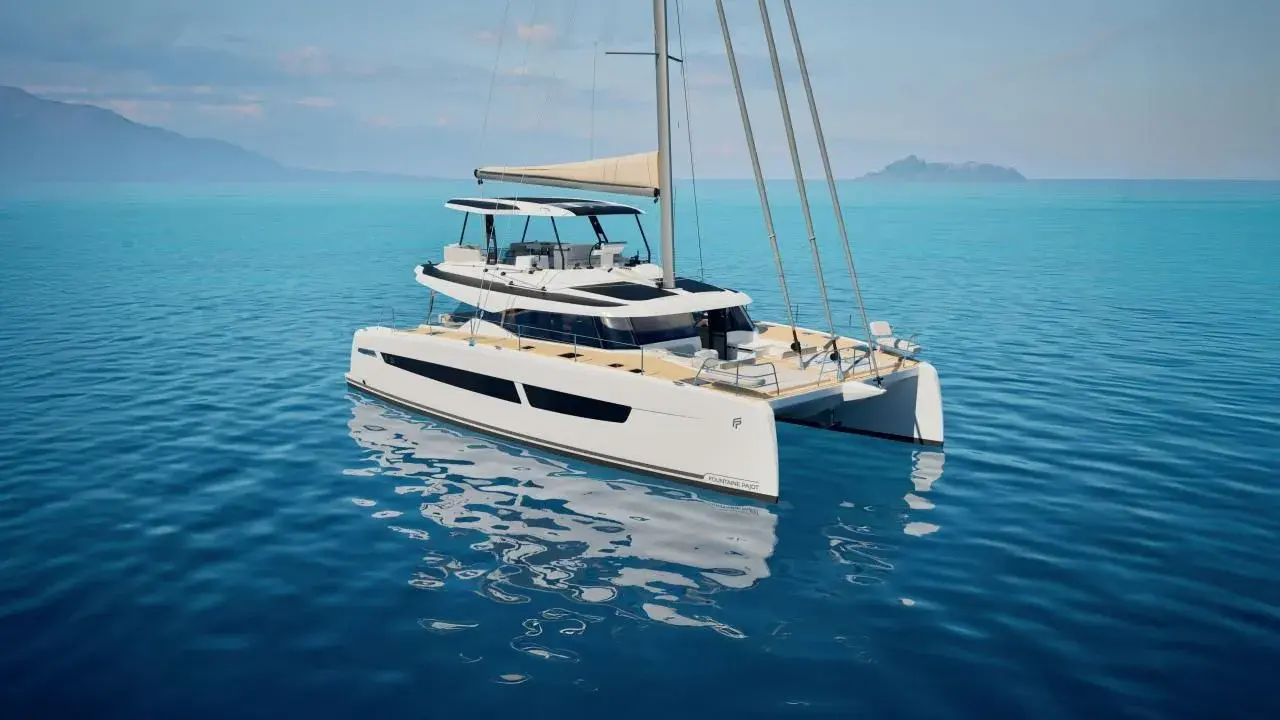 Eine weiße Katamaran-Yacht, eine FOUNTAINE PAJOT, gleitet auf ruhigem, blauem Wasser. Im Hintergrund sind Berge und eine Insel zu sehen.