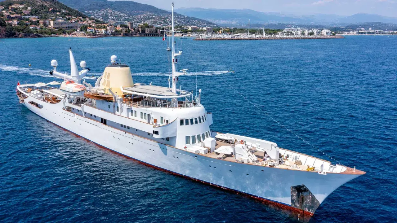 Die Christina O., eine luxuriöse Yacht, gleitet auf dem azurblauen Meer vor einer Küstenstadt.