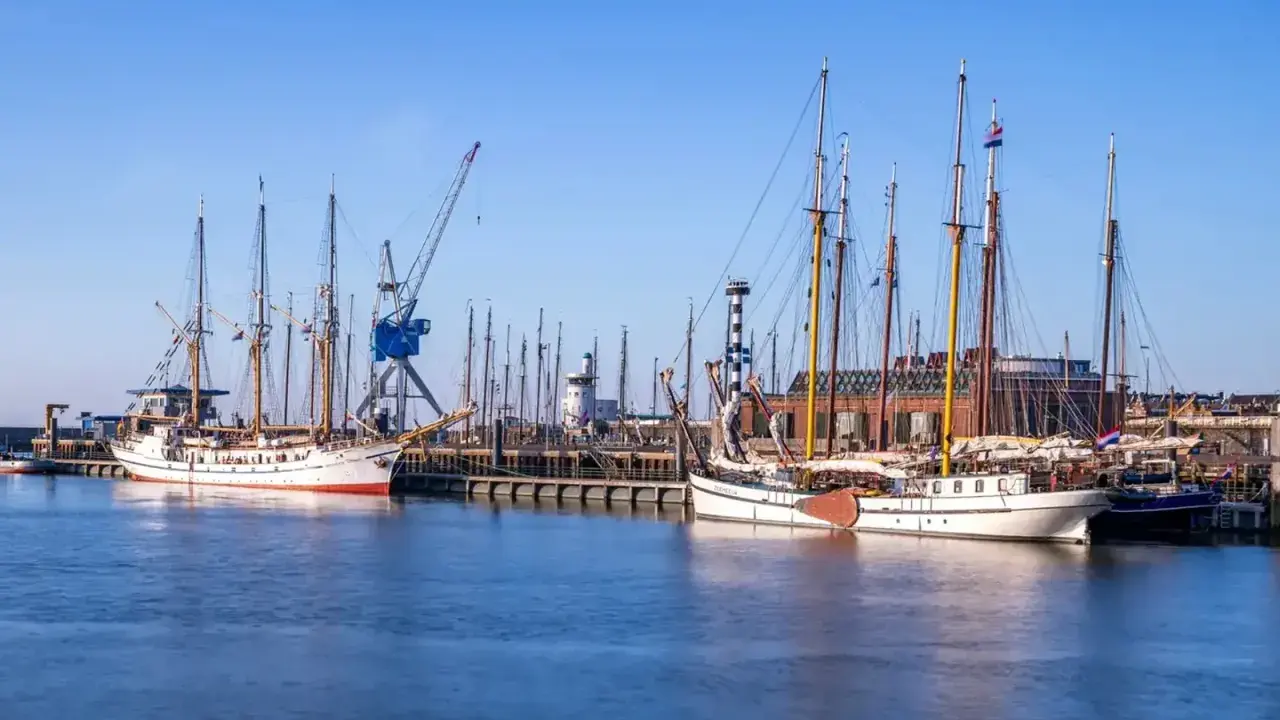 Segelschiffe im Harlingen Hafen, ein Kran ragt in den blauen Himmel.