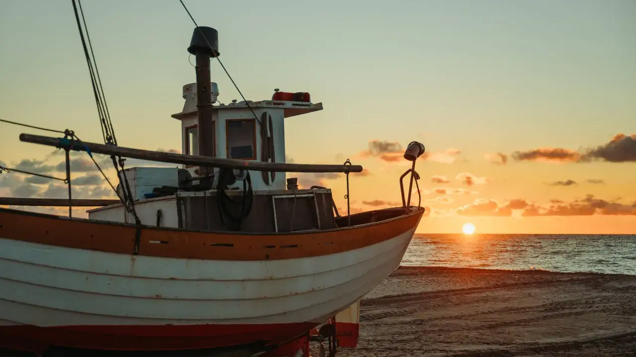 Ein Fischerboot liegt am Strand, während die Sonne im Meer versinkt. Der Unterschied zwischen einem Schiff und einem Boot wird hier deutlich: Dieses kleine Boot ist bereit für die nächste Fahrt.