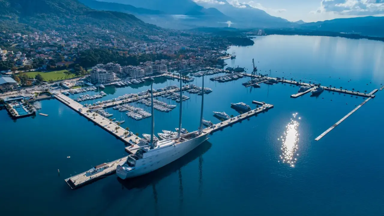 Ein riesiges Segelschiff liegt im porto hafen, umgeben von vielen Yachten und einer Stadt am Fuße von Bergen.