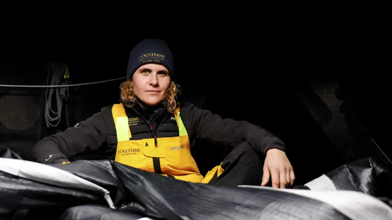 Clarisse Crémer, Seglerin im L'Occitane Sailing Team, sitzt in dunkler Kleidung und gelber Latzhose inmitten von Segeln.
