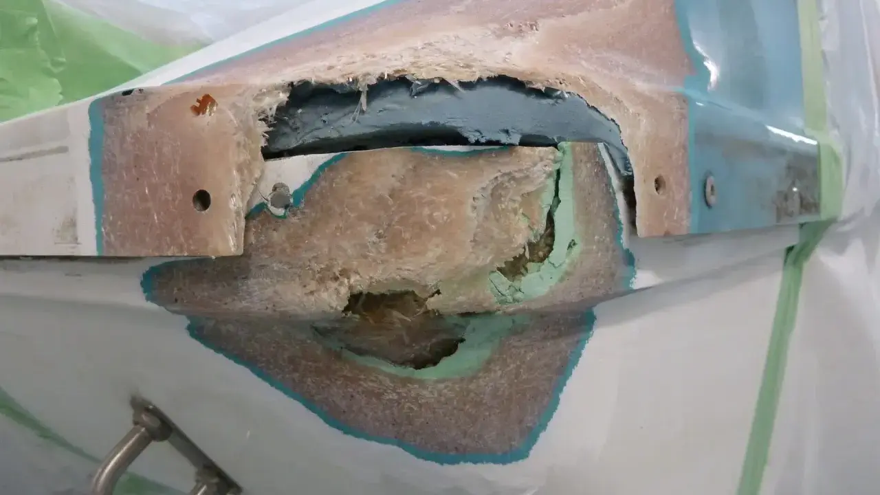 Beschädigte Stelle an einem GFK Boot, bereit für die Reparatur. Die Fasern sind freigelegt, ein Zeichen für notwendige Instandsetzung.