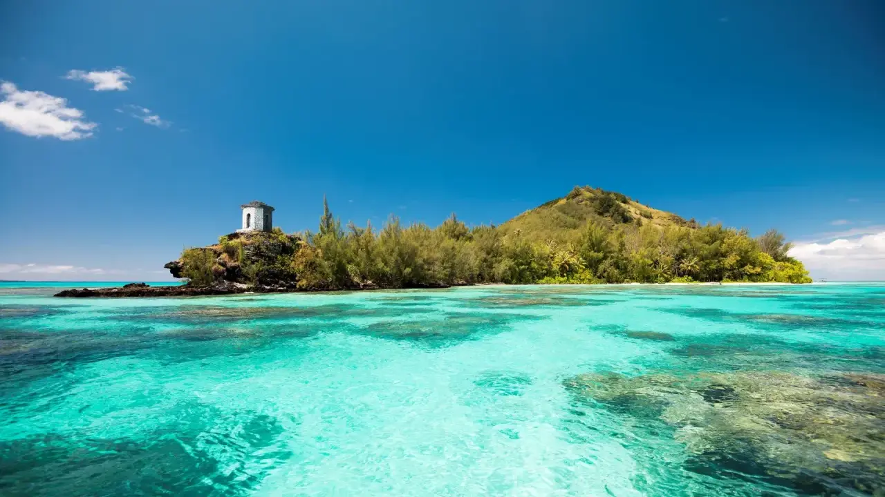 Türkisblaue Lagune vor den Gambierinseln mit einem kleinen Turm auf einer Felsinsel.