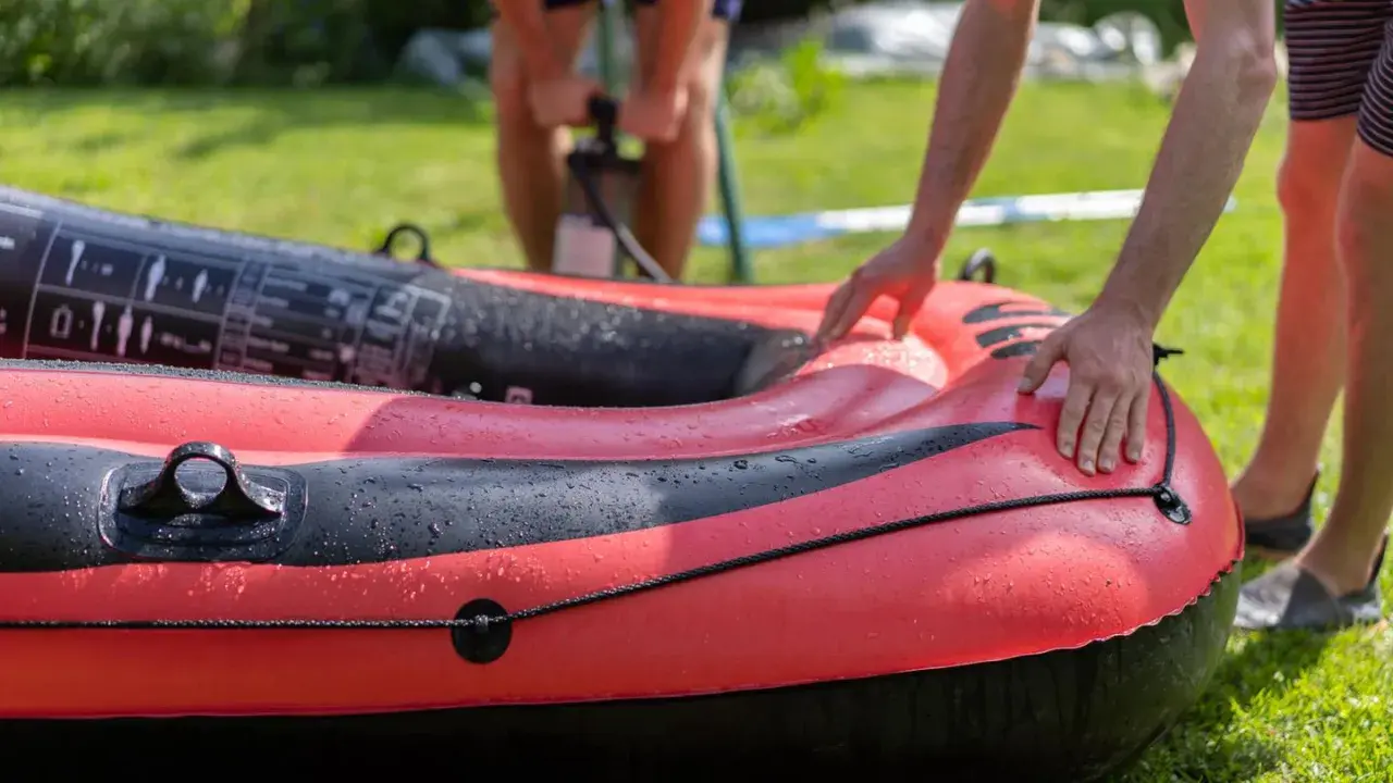 Hände bereiten das Schlauchboot vor, während im Hintergrund jemand pumpt.