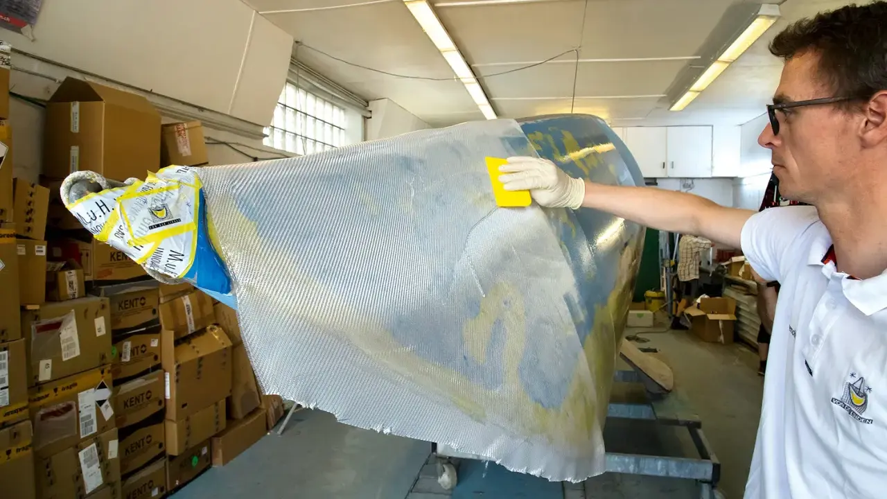 Mann bearbeitet mit gelbem Werkzeug und Handschuh ein Bootsteil. Epoxidharz Bootsbau-Material wird aufgetragen.