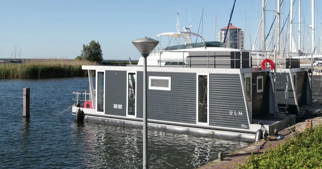 Modernes Hausboot "ULM" im lelystad hafen, umgeben von Schilf und Segelbooten.