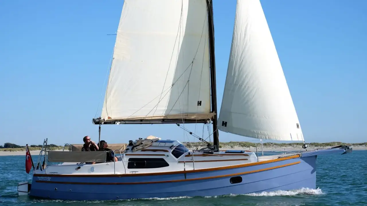 Eine blaue Baycruiser 26 segelt auf ruhigem Wasser unter klarem Himmel. Zwei Personen genießen die Fahrt.