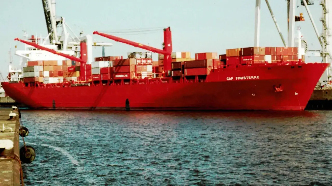 Rotes Containerschiff "Cap Finisterre" im Hafen, beladen mit vielen Containern, Kräne im Hintergrund.