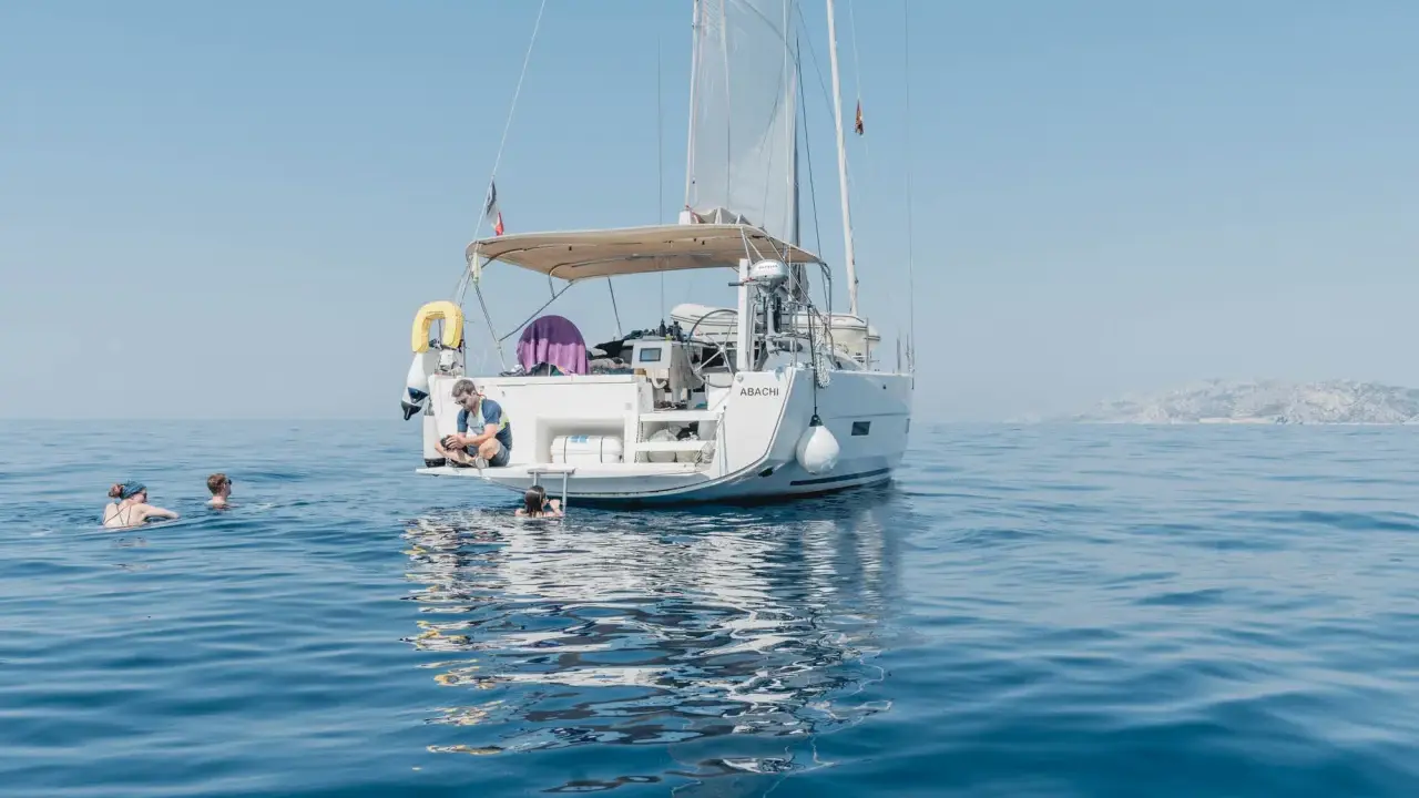 Erfahrungen, wenn du der Crew beitrittst: Ein Mann sitzt auf einer Yacht, während andere im Meer schwimmen.