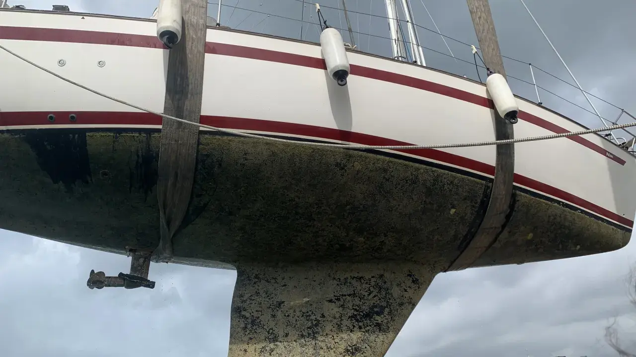 Segelboot wird angehoben, der Rumpf ist mit Algen bedeckt und bereit für die Behandlung mit Epoxidharz zum Streichen.