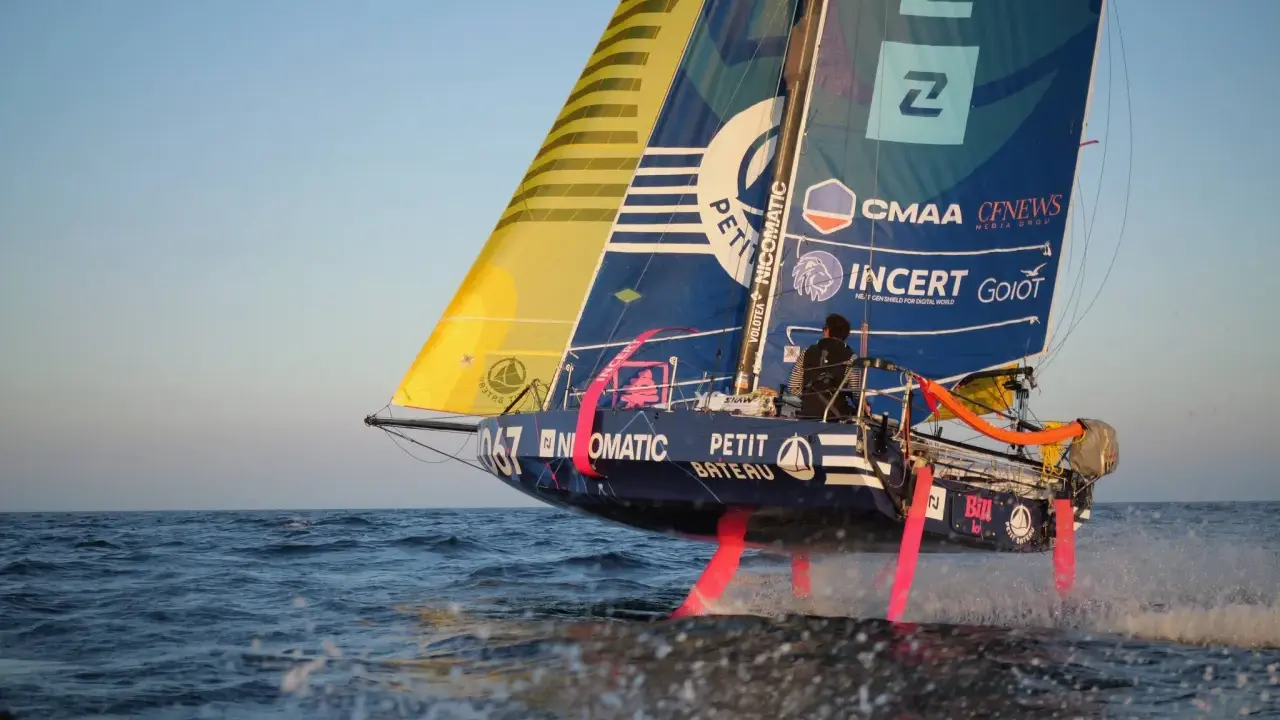 Segelboot mit pinken Foils rast über die Wellen. Ein Skipper steuert das Boot bei der Mini Transat Regatta.
