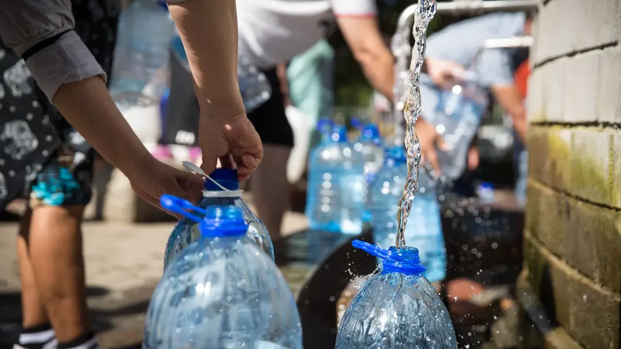 Menschen füllen Wasser in große Plastikflaschen. Die Frage, wie lange bleibt Wasser im Kanister frisch, ist hier relevant.