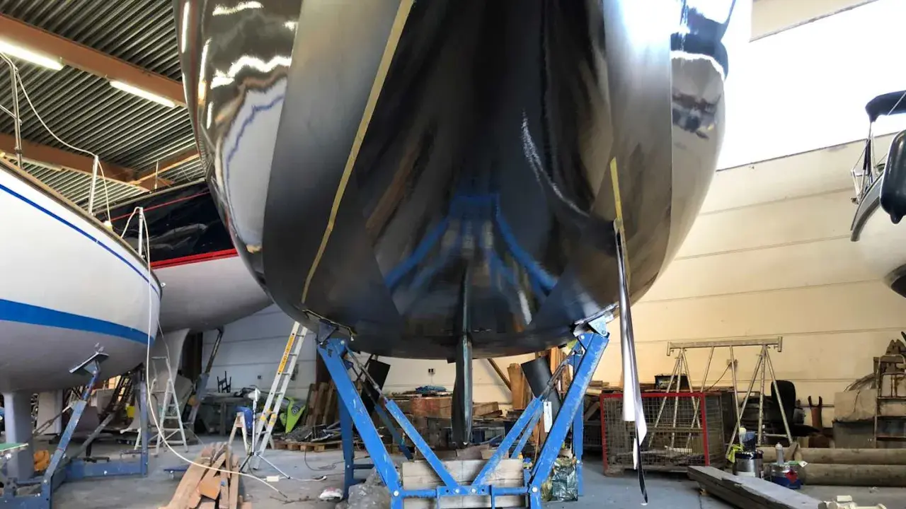Schwarzer Bootsrumpf auf Stützen, bereit für den antifouling test. Glänzende Oberfläche reflektiert die Werkstatt.