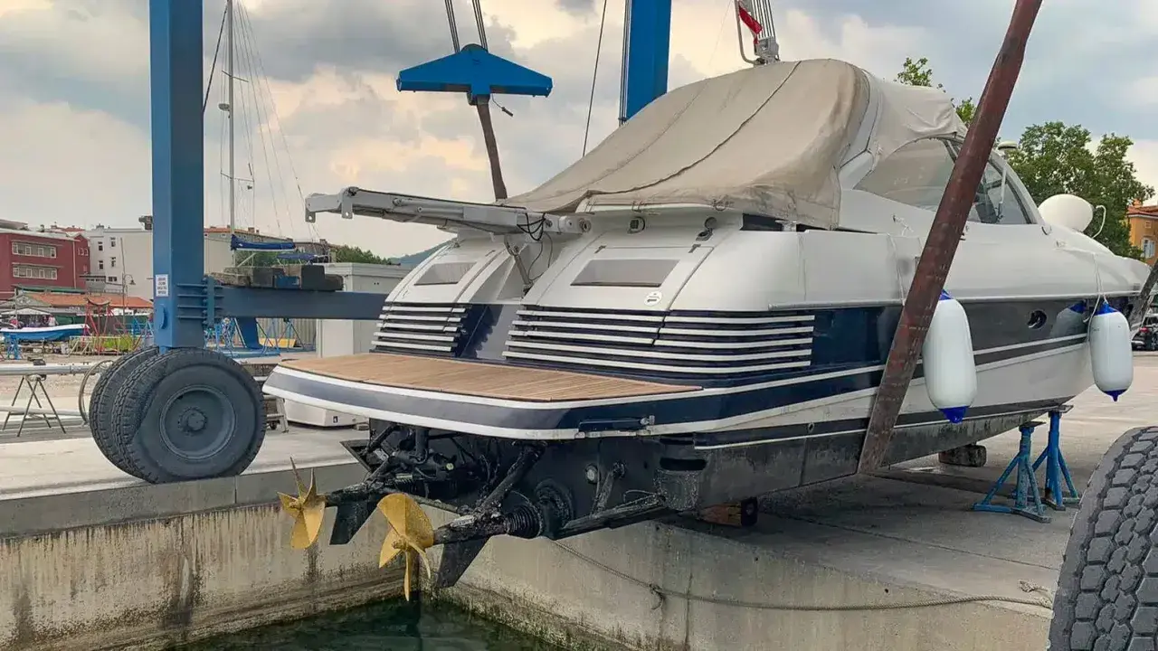 Ein luxuriöses Motorboot wird für das Winterlager aus dem Wasser gehoben. Zwei goldene Propeller ragen aus dem Rumpf.