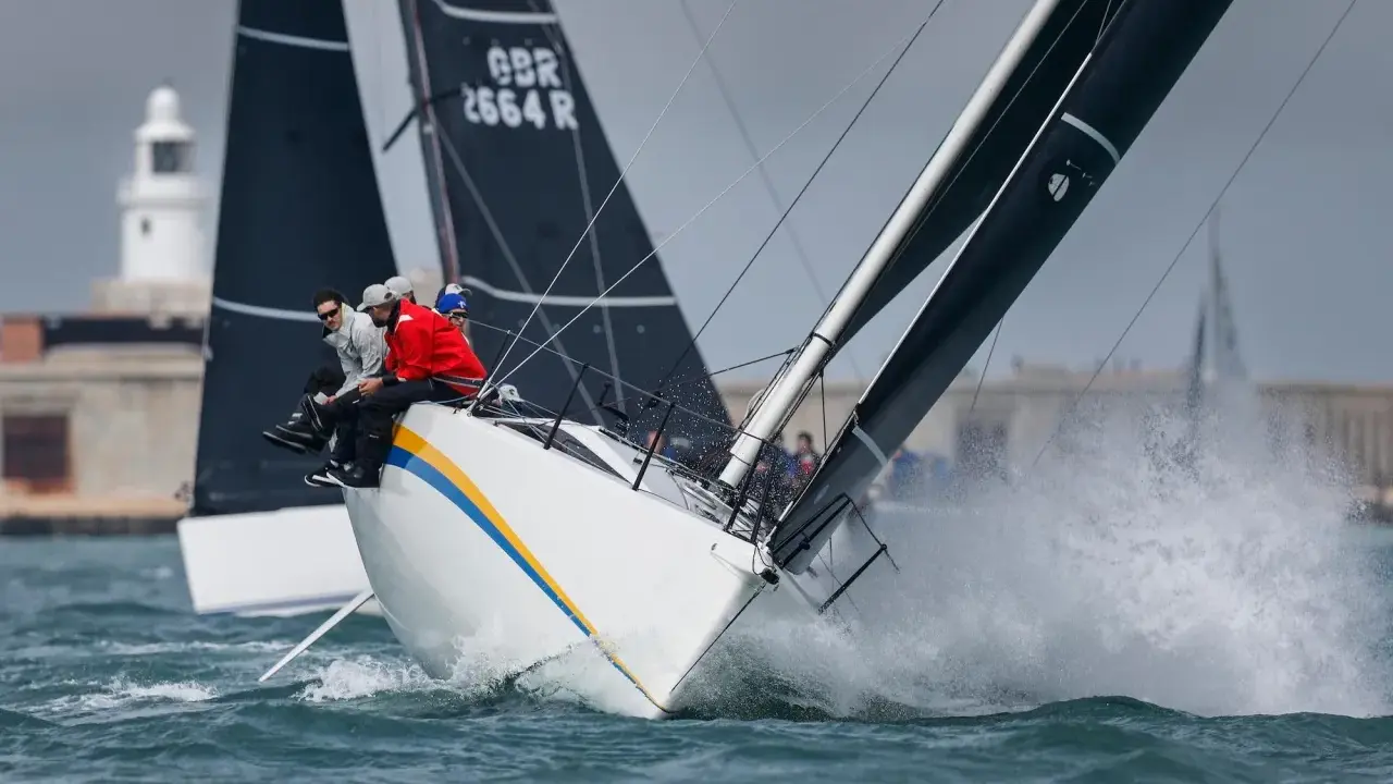 Segelboote kämpfen bei der Admirals Cup Regatta um die Wette. Gischt spritzt, die Crew sitzt tief.