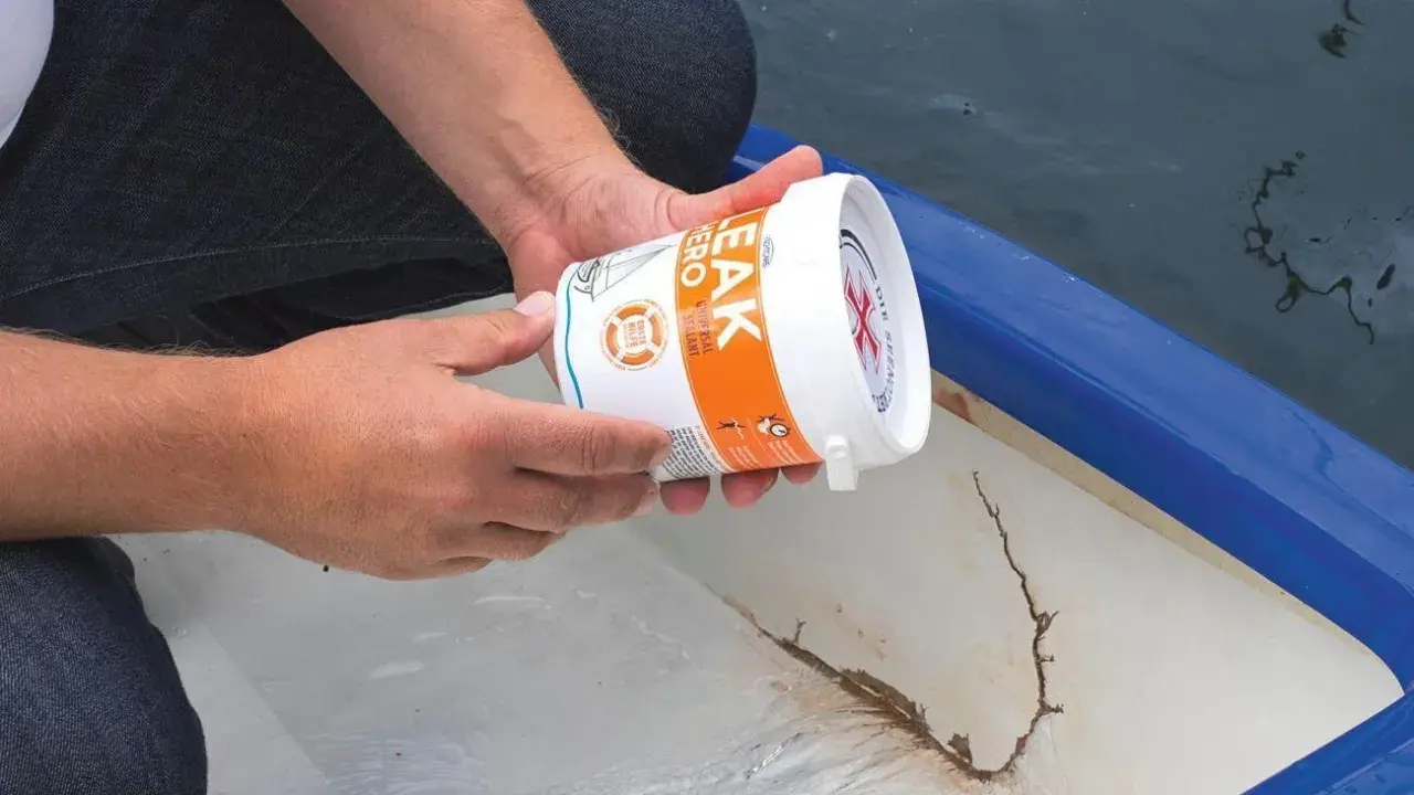 Person hält Dose mit Dichtmittel, um ein Boot abzudichten. Riss im Bootsrumpf sichtbar.