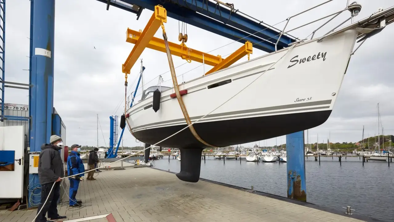Segelboot "Sweety" wird für das unterwasserschiff reinigen aus dem Wasser gehoben. Männer sichern das Boot mit Seilen.