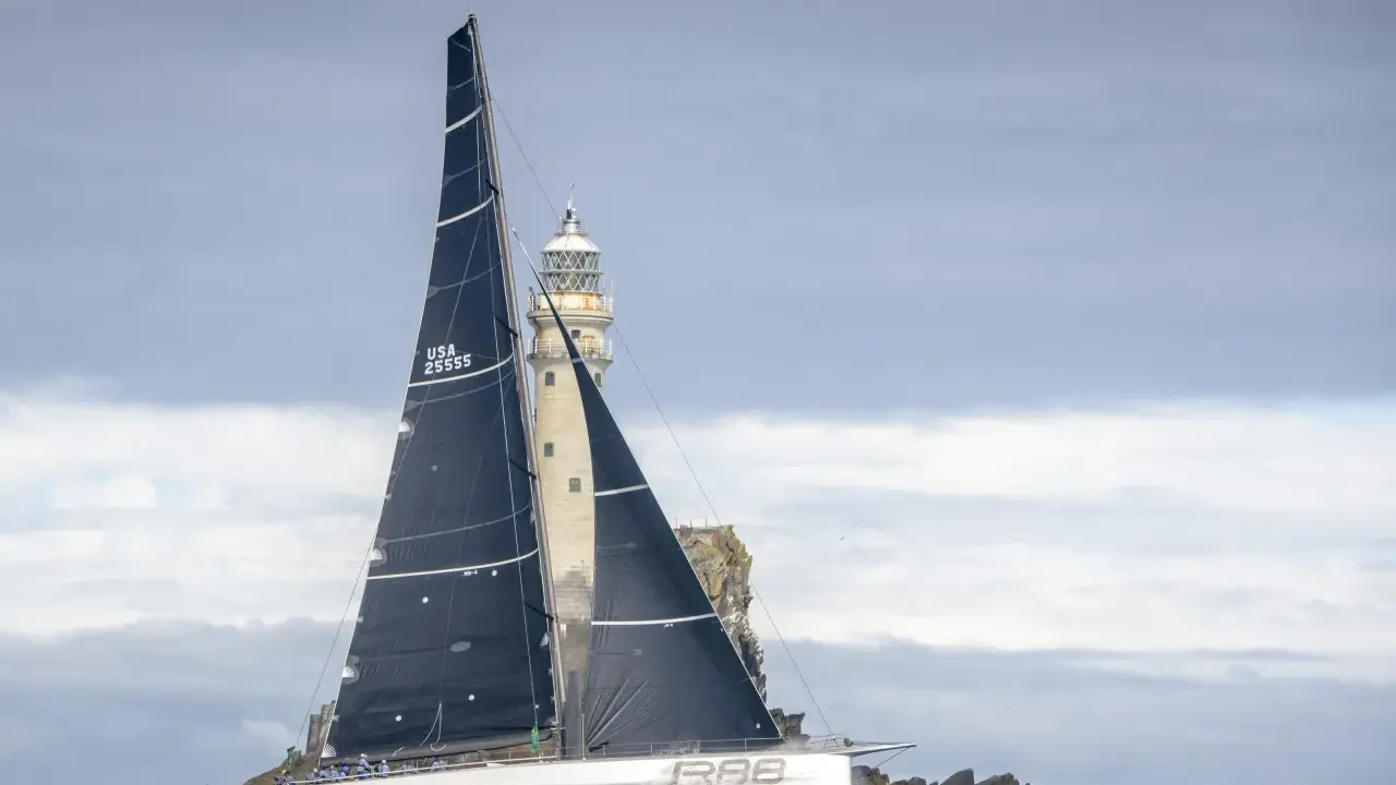 Segelboot mit schwarzen Segeln navigiert durch raue See am Fastnet Rock, ein dramatischer Moment im Fastnet Race.