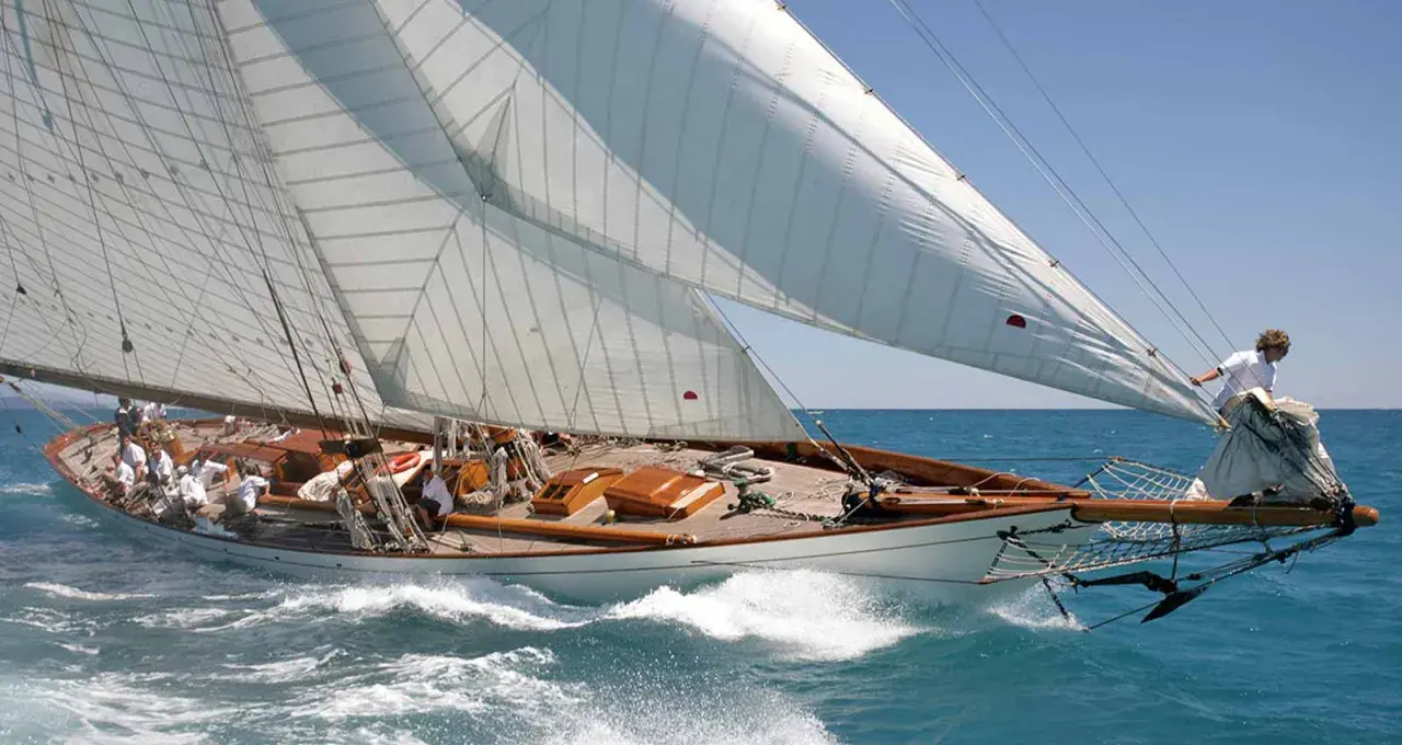 Eine elegante 12mr Yacht gleitet über das türkisfarbene Meer, die weißen Segel strahlen in der Sonne.