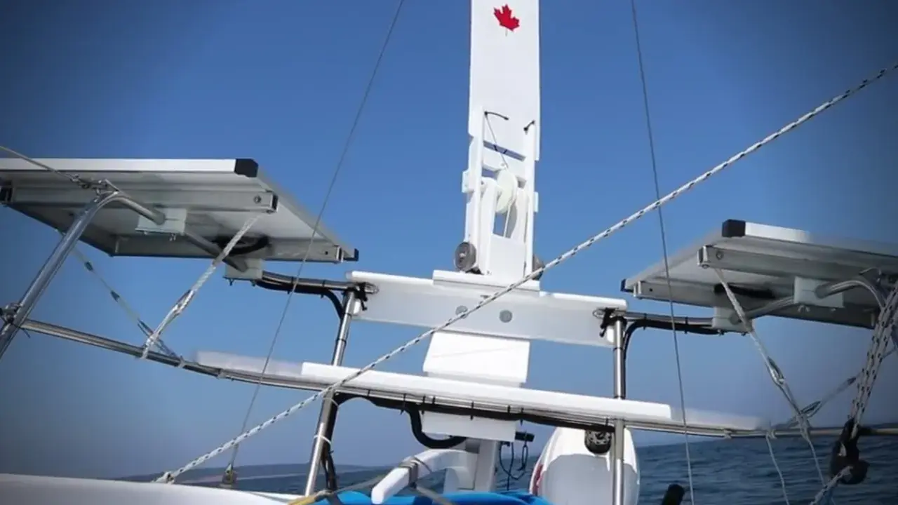Weiße Windfahne mit kanadischer Flagge auf einem Segelboot, mit Solarpaneelen und dem blauen Himmel im Hintergrund.