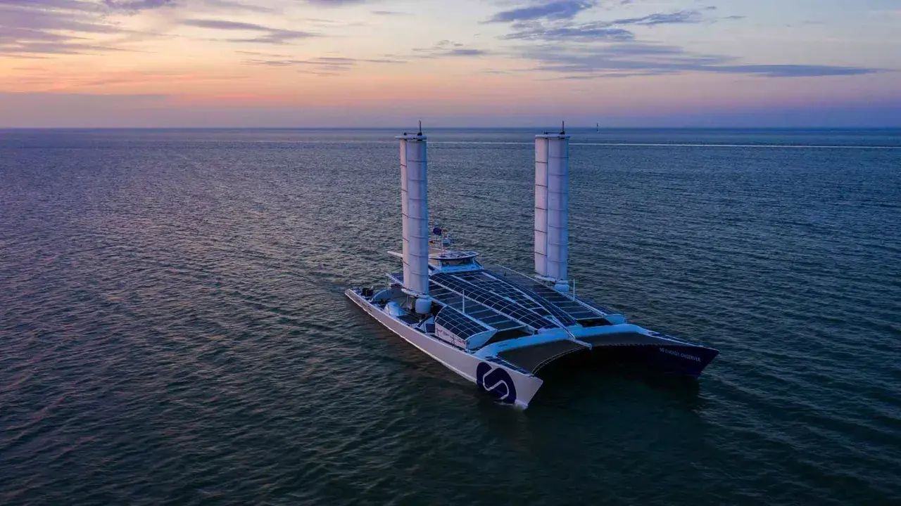 Der ENERGY OBSERVER, ein futuristisches Schiff mit Solarpaneelen und Windturbinen, gleitet bei Sonnenuntergang über das Meer.