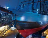 Ein historisches **fram schiff** mit Anker, umgeben von Treppen und Ausstellungsbereichen, in blauem Licht.