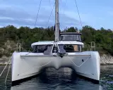Ein moderner Katamaran mit zwei Rümpfen, der wie ein schwimmendes Haus aussieht, ankert vor einer bewaldeten Küste.