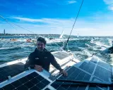 Boris Herrmann in Kiel, auf seinem Boot mit Solarpaneelen, umgeben von anderen Booten und Segelschiffen auf dem Meer.