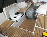 Ein weißes **Segelboot Toilette** mit offenem Deckel, daneben ein grauer Tank. Holzdecks und weiße Wände.