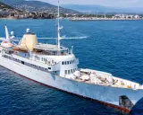 Die Christina O., eine luxuriöse Yacht, gleitet auf dem azurblauen Meer vor einer Küstenstadt.