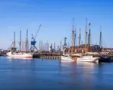 Segelschiffe im Harlingen Hafen, ein Kran ragt in den blauen Himmel.