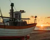 Ein Fischerboot liegt am Strand, während die Sonne im Meer versinkt. Der Unterschied zwischen einem Schiff und einem Boot wird hier deutlich: Dieses kleine Boot ist bereit für die nächste Fahrt.