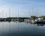 Segelboote und Motorboote liegen friedlich im Hafen Neuendorf, ihre Spiegelbilder tanzen auf dem ruhigen Wasser.