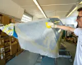 Mann bearbeitet mit gelbem Werkzeug und Handschuh ein Bootsteil. Epoxidharz Bootsbau-Material wird aufgetragen.