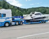 Ein LKW transportiert eine weiße Yacht auf einem Tieflader. Informieren Sie sich über bootstransport kosten für Ihre nächste Überführung.