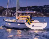 Eine Hallberg-Rassy 69 gleitet bei Dämmerung über das Wasser, die schwedische Flagge weht im Wind.