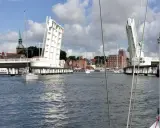 Eine Klappbrücke öffnet sich für Segelboote in Kappeln an der Schlei. Im Hintergrund die Stadt mit Kirchturm und Backsteingebäuden.