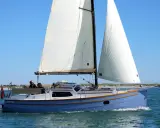 Eine blaue Baycruiser 26 segelt auf ruhigem Wasser unter klarem Himmel. Zwei Personen genießen die Fahrt.