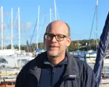 Mann mit Brille lächelt vor Segelbooten. Henningsen und Steckmest sind bereit für die nächste Ausfahrt.