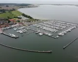 Maasholm Hafen mit vielen Segelbooten und Yachten, die an Stegen liegen. Im Hintergrund ein Dorf und das weite Wasser.