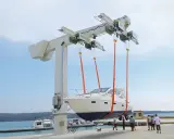 Ein großer Kran hebt ein weißes Boot aus dem Wasser. Mehrere Personen beobachten den Vorgang.