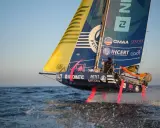 Segelboot mit pinken Foils rast über die Wellen. Ein Skipper steuert das Boot bei der Mini Transat Regatta.