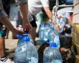 Menschen füllen Wasser in große Plastikflaschen. Die Frage, wie lange bleibt Wasser im Kanister frisch, ist hier relevant.