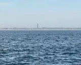 Der Leuchtturm Norderney ragt über die Dünenlandschaft am Horizont. Das weite Meer liegt davor.